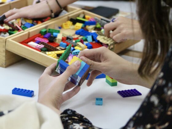 Fotografía a color en posición horizontal que muestra las manos de dos personas construyendo modelos con bloques, en una dinámica con la metodología Lego Serious Play.