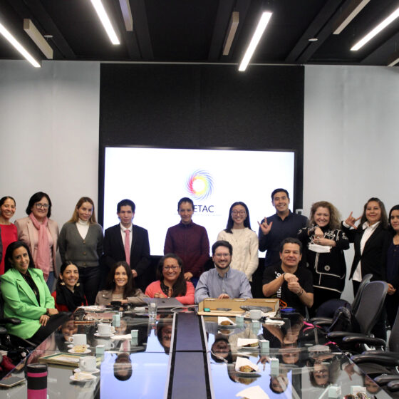 Fotografía de un grupo de personas con vestimenta formal en una sala de juntas. Algunas están de pie y otras sentadas volteando a ver a la cámara. Entre ellas se encuentran una persona con discapacidad visual y una con discapacidad auditiva, así como dos intérpretes de lengua de señas. Al fondo se aprecia una pantalla con el logotipo del IMETAC.