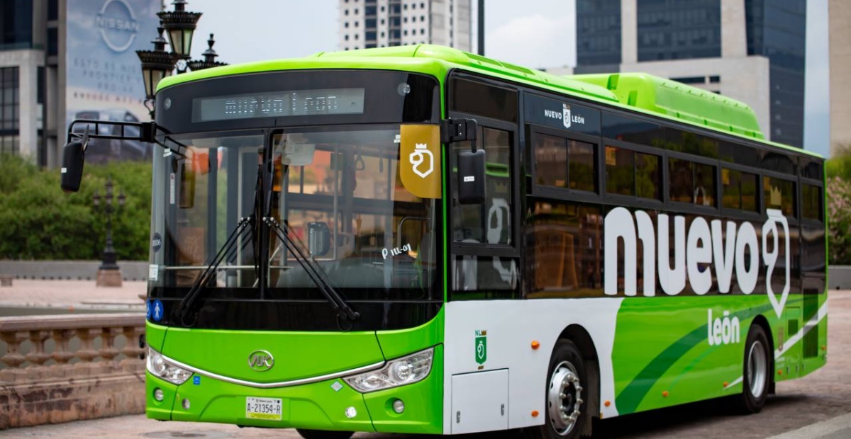 Fotografía de un autobús verde transitando por las calles de Monterrey, Nuevo León. En el lateral del autobús hay una franja verde oscuro y el texto "muevo león", a modo de juego de palabras con el nombre del estado. A su lado hay un icono con forma de león con corona.