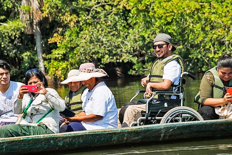 Fotografía de seis turistas de diferentes edades y nacionalidades, sobre una balsa en un río. Uno de los turistas va en la balsa sentado en una silla de ruedas.