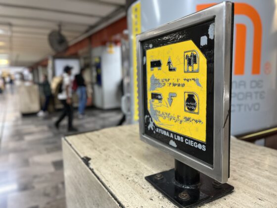 Fotografía de una placa con información en braille, que está sobre un murete en una estación del metro de la Ciudad de México. La placa se ve descuidada y despintada por el uso.