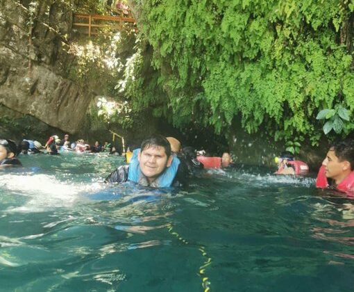 Fotografía de Luis Fernando nadando en la Poza Azul de Tamasopo. Trae un chaleco salvavidas. Al fondo se ven más personas nadando, vegetación y una pared de roca.