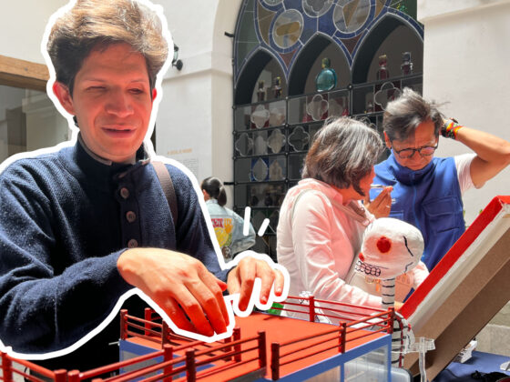 Foto de un hombre con discapacidad visual tocando una maqueta de la casa estudio Diego Rivera y Frida Kahlo. Atrás está una mujer con discapacidad visual tocando un cuadro con texturas en relieve. Un guía le intenta explicar de qué trata la obra, mientras se rasca la cabeza.