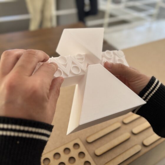 Foto de la réplica de una escultura de la ruta de la amistad, impresa en 3d, en las manos de un hombre con discapacidad visual. La escultura se forma de 2 triángulos, uno de cabeza arriba de uno normal, entre los que hay una franja rectangular con figuras estilo prehispánicas labradas en alto relieve.