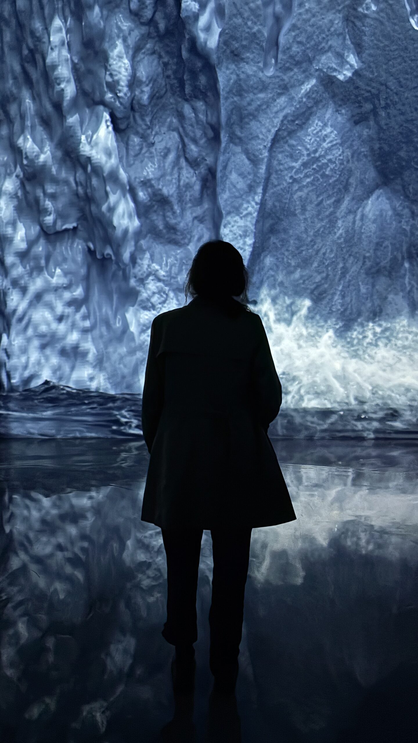 Foto vertical de una mujer de espaldas frente a una proyección de una cueva de hielo.
