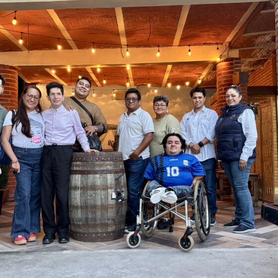 Foto horizontal de turistas con discapacidades motrices y visual, junto con guías de turistas posando durante la visita a una vinícola.