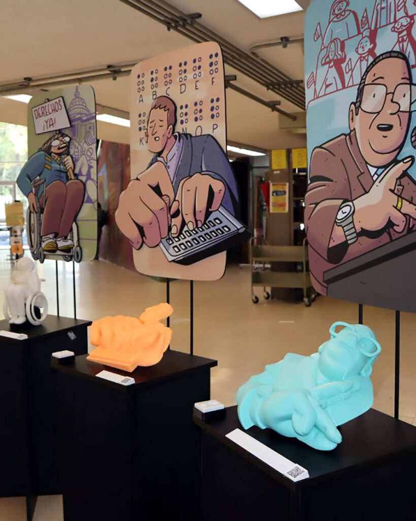 Fotografía de la exposición “los muros que derribamos” montada en una biblioteca, en el CCH Azcapotzalco. Se ven 3 pedestales con figuras impresas en 3D de personajes con discapacidad importantes a lo largo de la historia: Gilberto Rincón Gallardo, Louis Braille y Judith Heumann. Cada pedestal tiene también una ilustración en gran formato de cada personaje, cédulas en braille y bocinas donde se pueden escuchar sus respectivas audioguías.